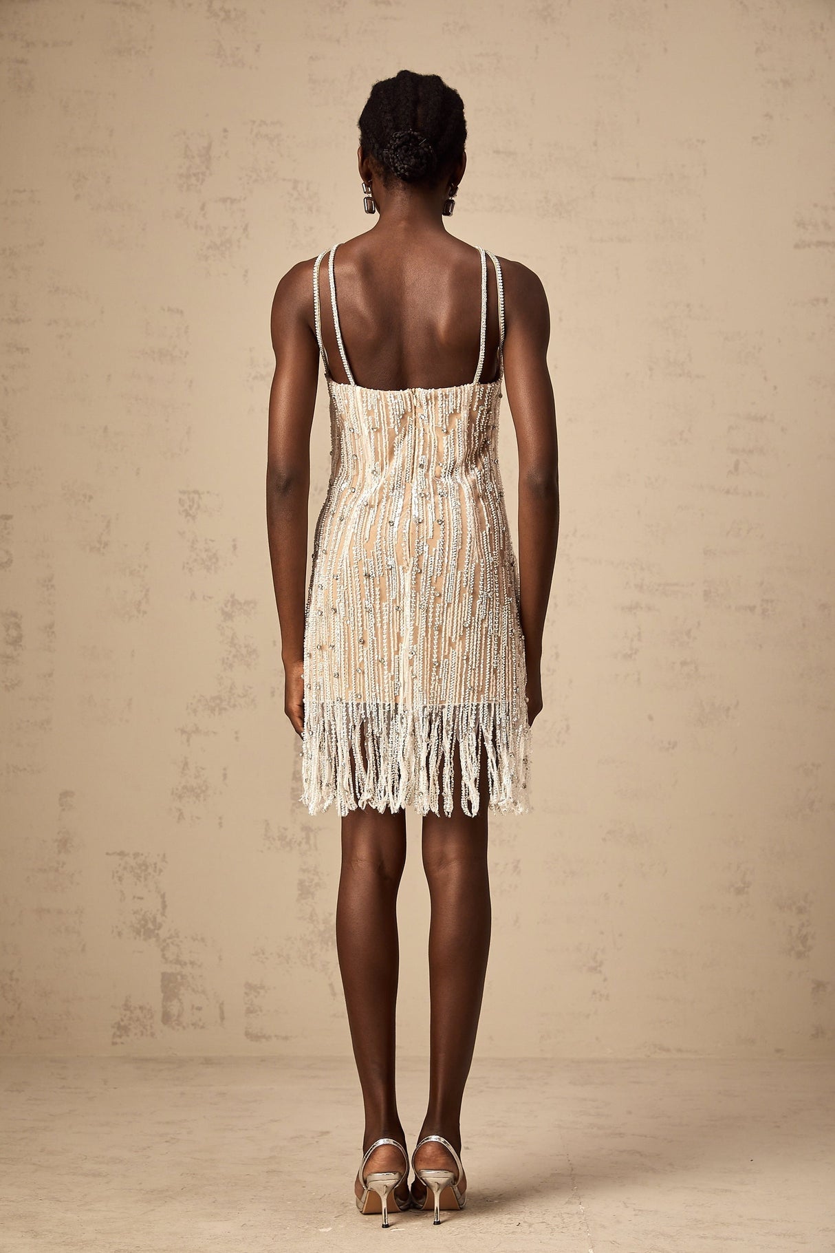 Woman wearing short black dress with sparkly embellishments and fringe details at hem