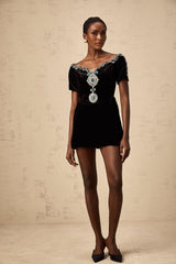 Woman wearing short black velvet dress with embellishments and thin straps