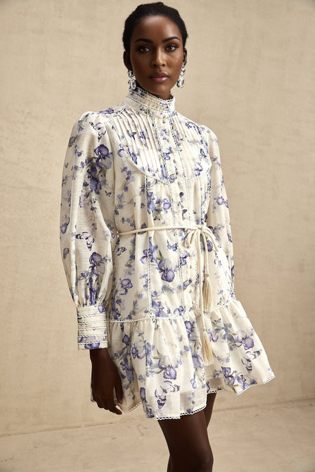 Woman wearing short floral print dress with flared skirt and chiffon fabric in pastel colors against plain background