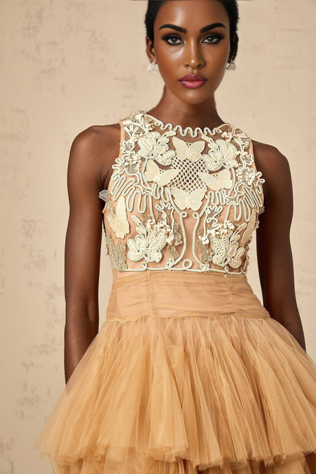 Woman wearing short khaki dress with lace panels and embellishments standing against plain background
