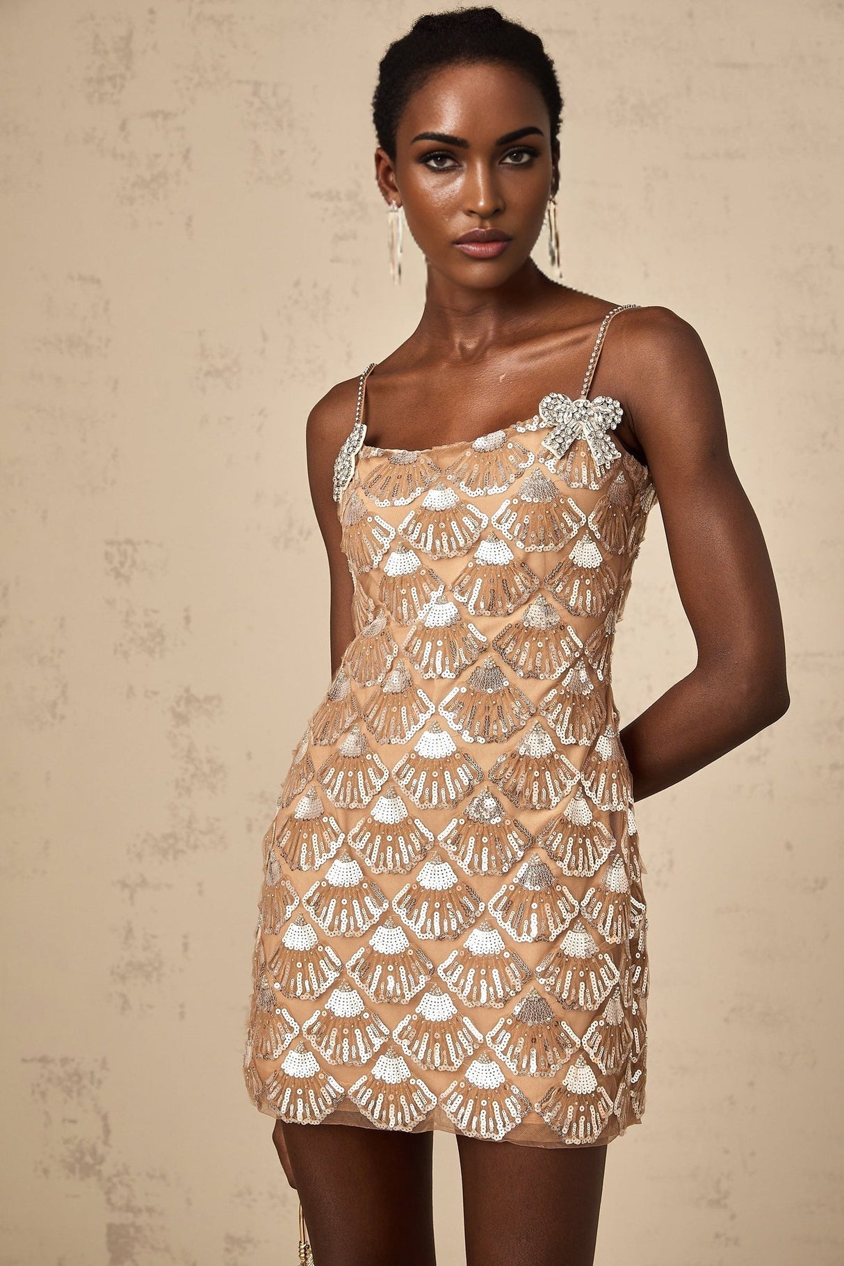 Woman wearing short sparkly gold dress with long sleeves and high neckline