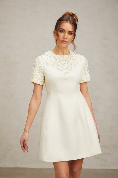 Woman wearing short white dress with colorful floral applique details and puff sleeves