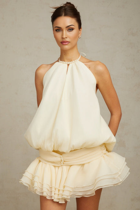 Woman wearing short white halterneck dress with faux pearl details