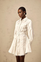 Woman wearing short white shirt dress with belt cinched at waist