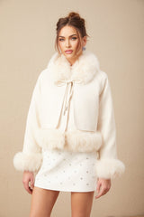 Woman wearing short white suede coat with fur trim and padded design standing against plain background