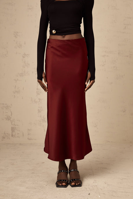 Woman wearing vibrant red satin skirt with flared silhouette against plain background