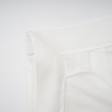 Woman wearing white creased top and matching trousers set standing against plain background