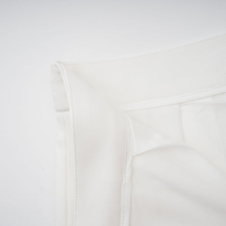 Woman wearing white creased top and matching trousers set standing against plain background