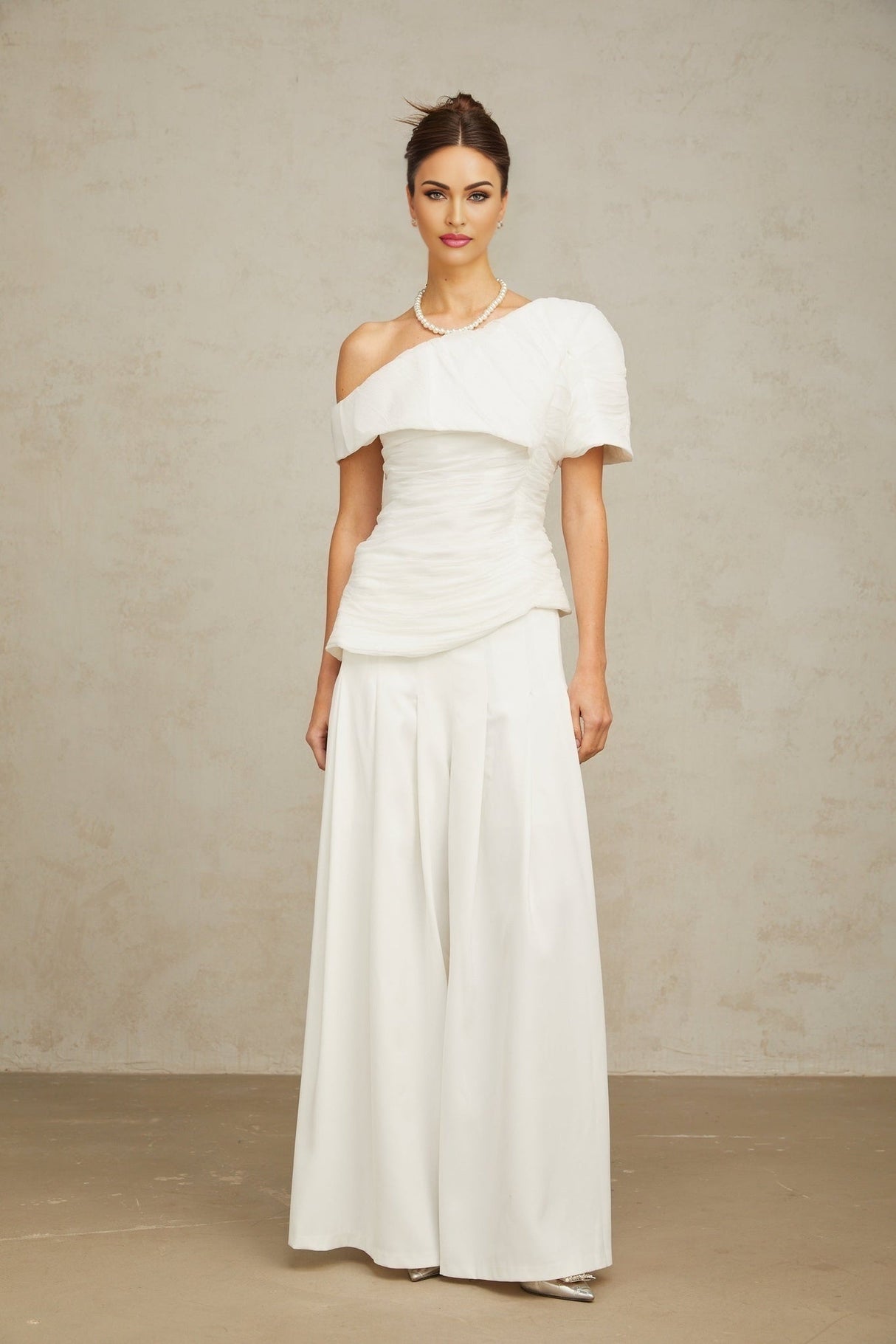 Woman wearing white creased top and matching trousers standing in relaxed pose