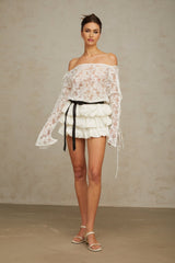 Woman wearing white floral lace top and matching skirt set standing against plain background