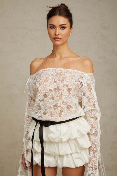 Woman wearing white floral lace top and matching skirt set standing against plain background