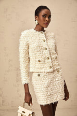 Woman wearing white fuzzy knit cardigan and matching skirt set against plain background