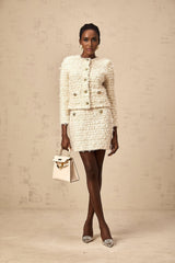 Woman wearing white fuzzy knit cardigan and matching skirt set standing against plain background