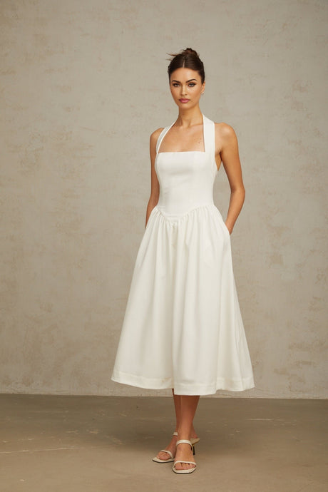 Woman wearing white halterneck pleated midi dress standing against neutral background