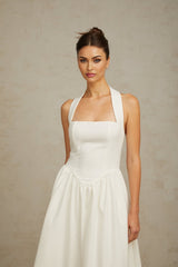 Woman wearing white halterneck pleated midi dress standing against plain background
