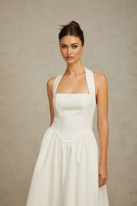 Woman wearing white halterneck pleated midi dress standing against plain background