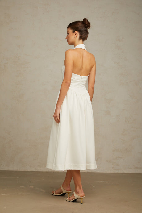 Woman wearing white halterneck pleated midi dress with fitted waist and flowy skirt