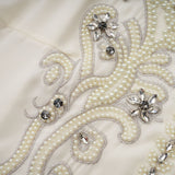 Woman wearing white jacket and dress set with pleated details and embellishments