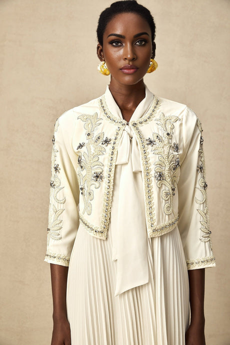 Woman wearing white jacket and dress set with pleated details and embellishments