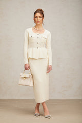 Woman wearing white knitted crop top and matching midi skirt standing against plain background
