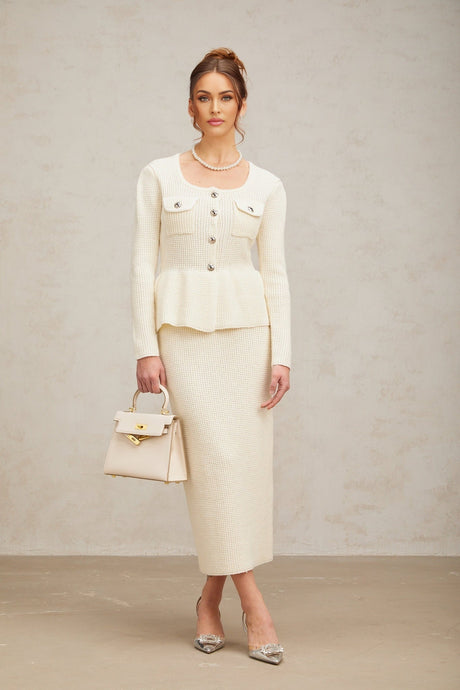 Woman wearing white knitted crop top and matching midi skirt standing against plain background