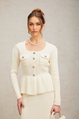 Woman wearing white knitted sleeveless top and matching knee length skirt standing against plain background