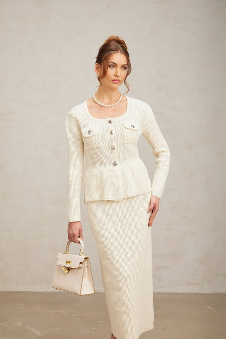 Woman wearing white knitted sleeveless top and matching midi skirt standing against plain background