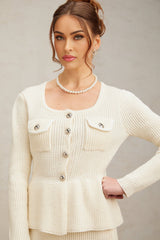 Woman wearing white knitted sleeveless top and matching skirt set standing against plain background