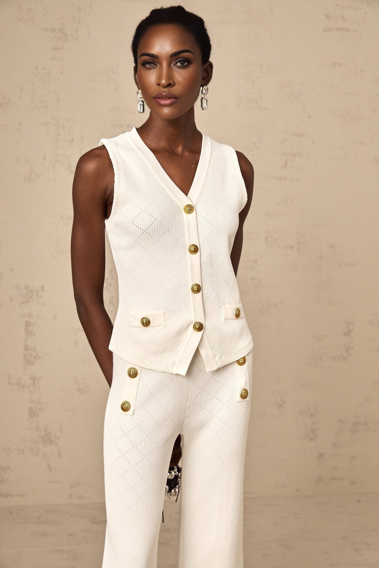 Woman wearing white knitted top and matching trousers standing against plain background