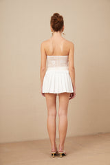 Woman wearing white lace crop top and matching high waisted skirt standing against plain background