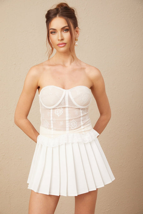 Woman wearing white lace matching set consisting of a top and skirt standing against plain background