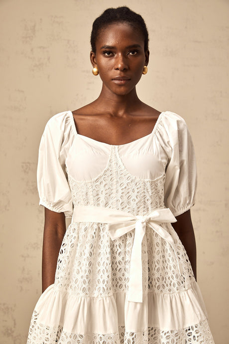 Woman wearing white lace midi dress with tiered skirt and corded lace details standing in front of neutral background