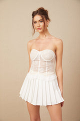 Woman wearing white lace top and matching skirt set against plain background
