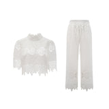 Woman wearing white lace trim cropped top and matching trousers set featuring cutout details