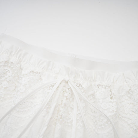 Woman wearing white lace trim cropped top and matching trousers set with cutout details