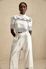 Woman wearing white lace trim cropped top and matching trousers with cutout details Raphaelle matching set