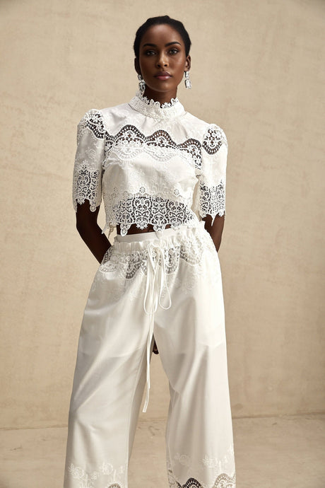 Woman wearing white lace trim cropped top and matching trousers with cutout details Raphaelle matching set