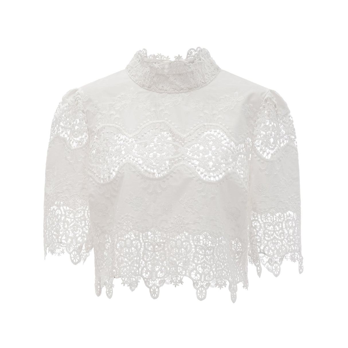 Woman wearing white lace trim cropped top and matching trousers with cutout details standing against plain background