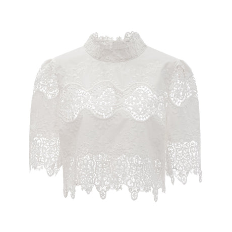 Woman wearing white lace trim cropped top and matching trousers with cutout details standing against plain background
