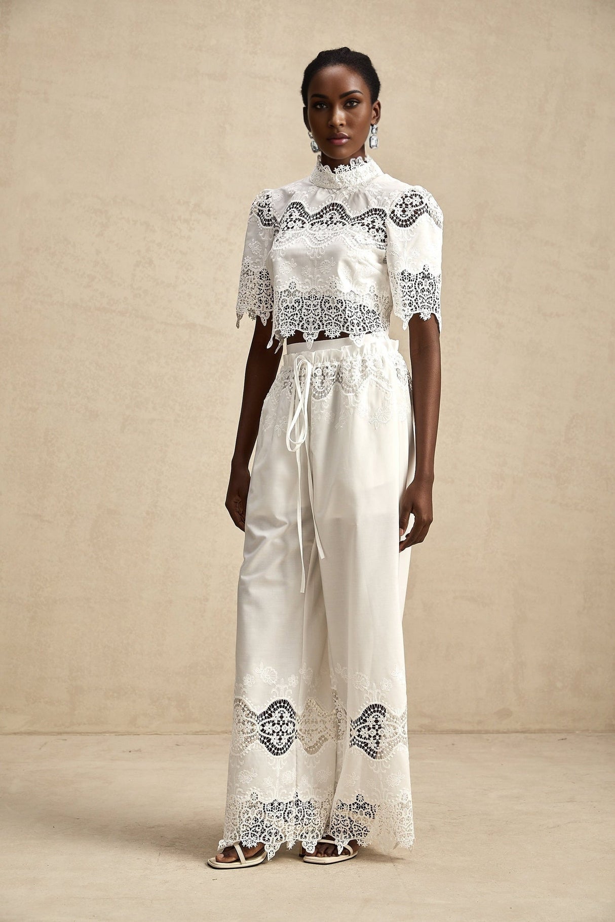 Woman wearing white lace trimmed cropped top and matching trousers set with cutout details