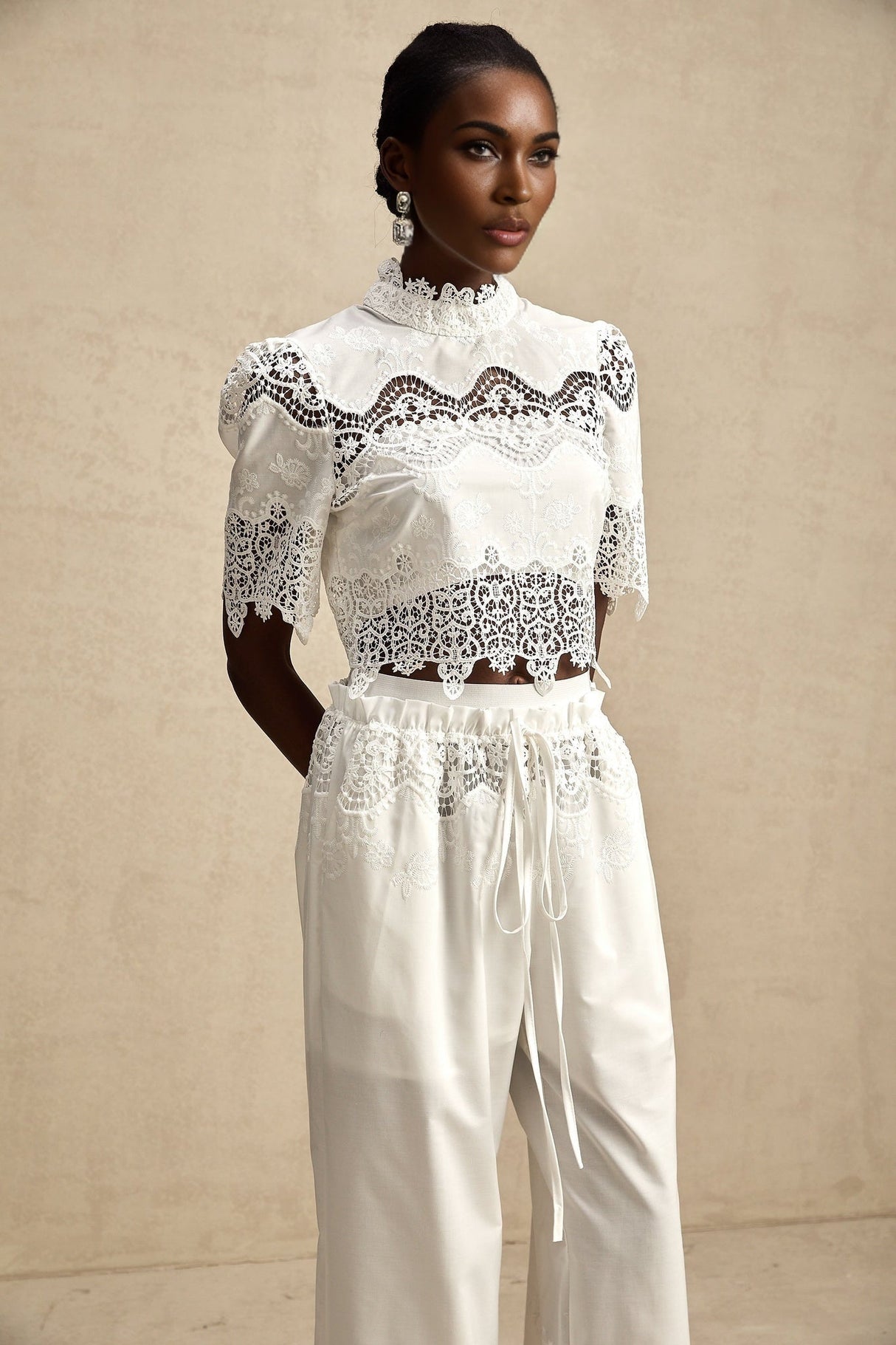 Woman wearing white lace trimmed cropped top and matching trousers with cutout details