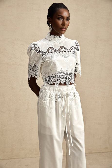 Woman wearing white lace trimmed cropped top and matching trousers with cutout details