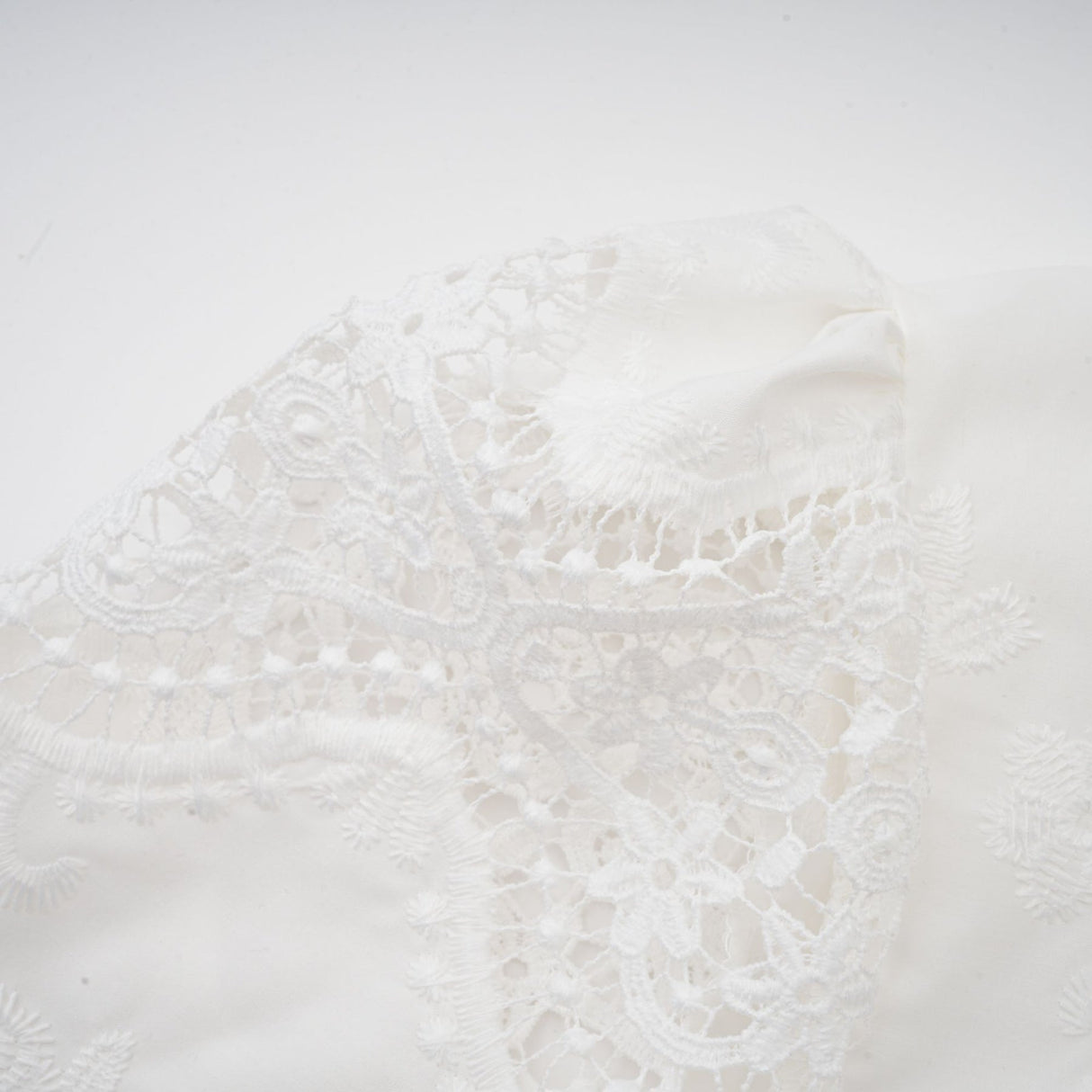Woman wearing white lace trimmed cropped top and matching trousers with cutout details