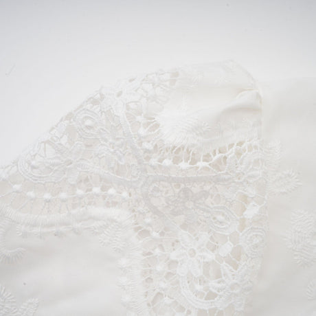 Woman wearing white lace trimmed cropped top and matching trousers with cutout details