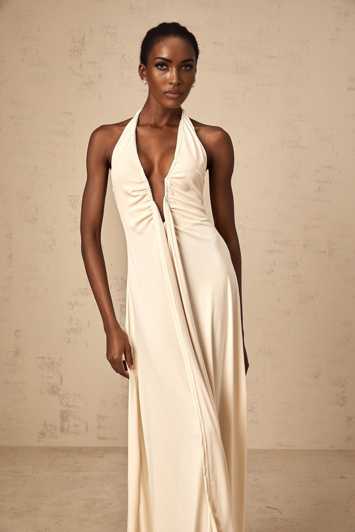 Woman wearing white long flowing maxi dress with deep V neckline and draped fabric detail