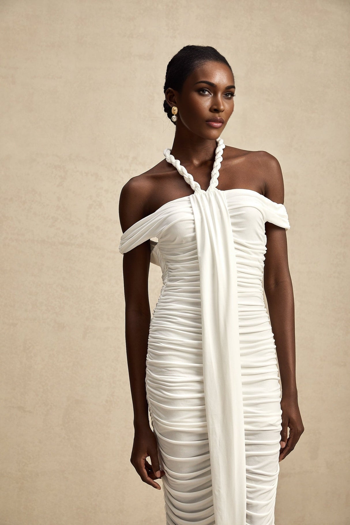 Woman wearing white midi dress with braided rope details and sleeveless design standing against plain background