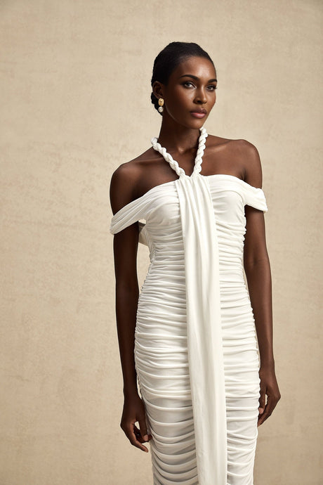 Woman wearing white midi dress with braided rope details and sleeveless design standing against plain background