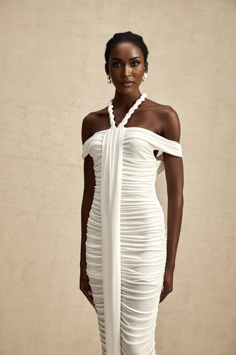 Woman wearing white midi dress with braided rope details on sleeves and waist standing against neutral background
