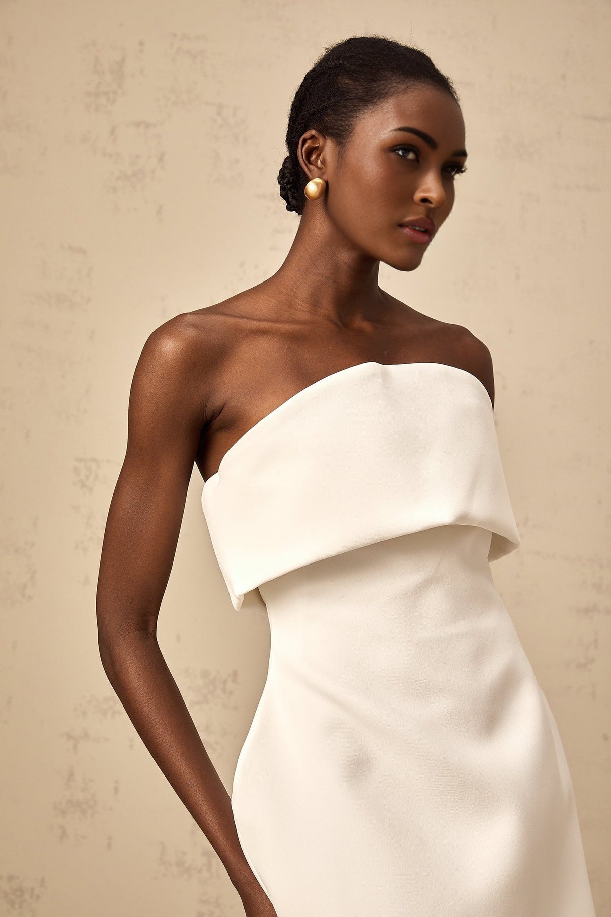 Woman wearing white offshoulder mini dress with puffed sleeves standing against plain background