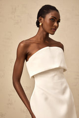 Woman wearing white offshoulder mini dress with puffed sleeves standing against plain background